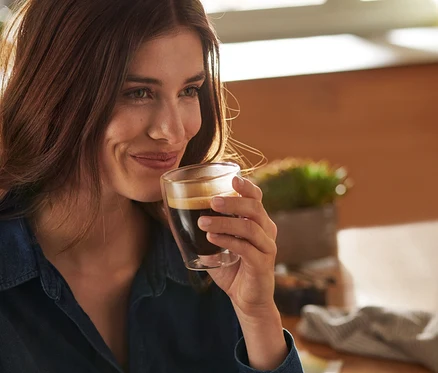 Lächelnde Frau hält ein doppelwandiges Caffè Crema Glas.