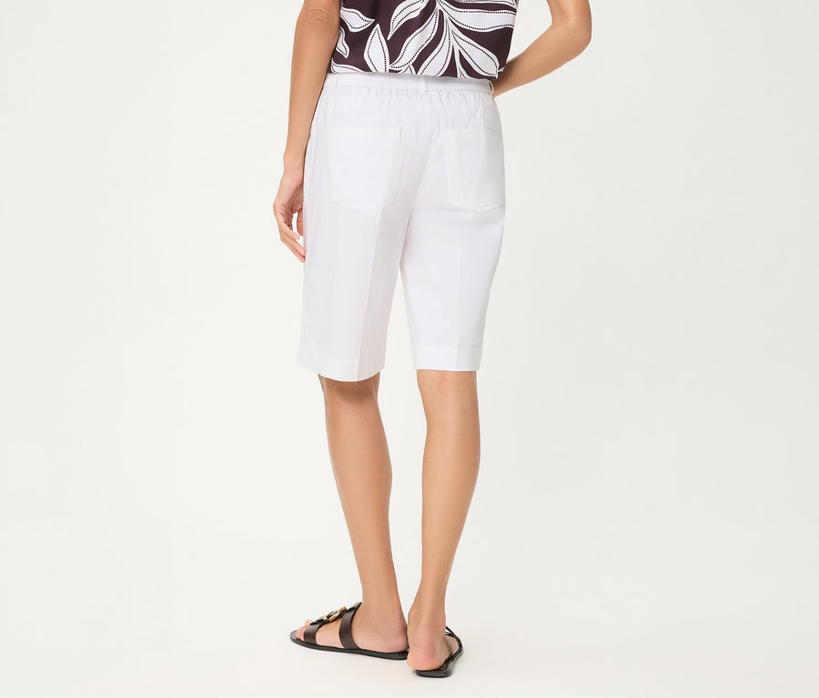 Person von hinten in weißen Olsen Shorts, einem gemusterten Oberteil und schwarzen Sandalen.