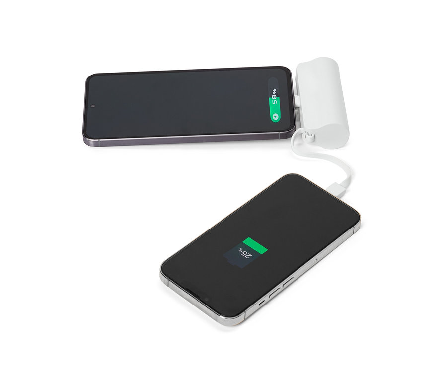 Zwei Smartphones, von denen eines mit einem weißen tragbaren Ladegerät verbunden ist, liegen auf einer weißen Oberfläche.