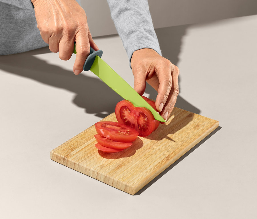 Frau schneidet Tomate mit grünem Messer aus Küchenhelfer-Set auf Holzbrettchen.
