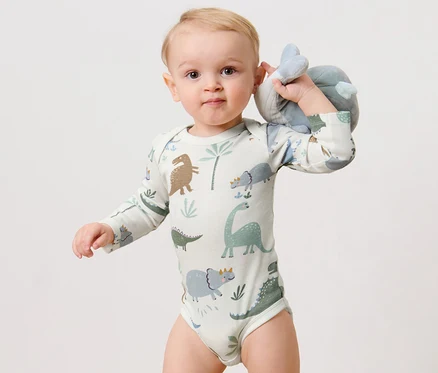 Ein Baby hält ein Stofftier und trägt einen 3 Langarmbodys, Dino.