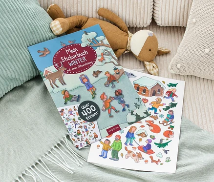 Auf einer Decke liegen das "Mein Stickerbuch »Winter«" und ein Stofftier.