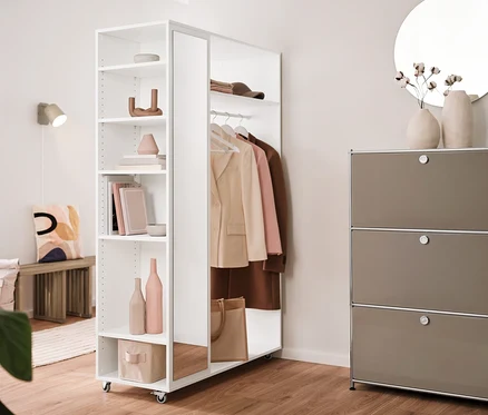 Einrichtung mit einer Ausziehbank, einer mobilen Spiegelschrank-Garderobe, einem Regal Metall »CN3« mit 3 Klappenfächern und einer cremefarbenen Wandleuchte aus Metall. Im Hintergrund hängt ein runder Spiegel »Ameca«.