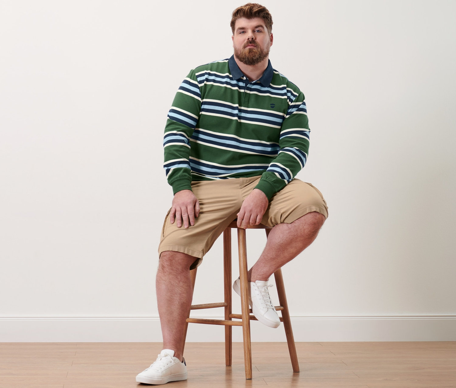 Mann sitzt auf Hocker, trägt Langarm-Poloshirt und Cargo-Shorts in Sand.