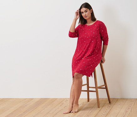 Frau sitzt auf einem Hocker und trägt ein rotes Nachthemd.