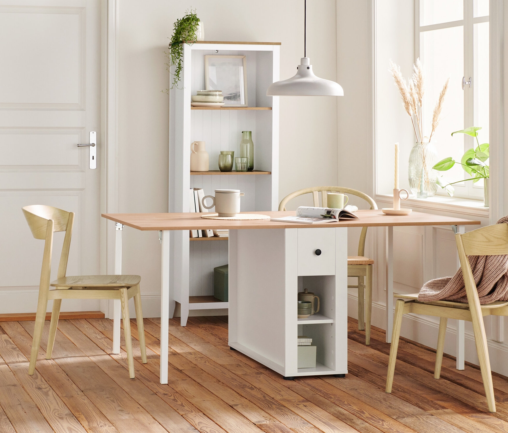 Innenraum mit Holzboden, Holzstuhl, Regal, Anrichte mit Schubladen und Tischleuchte mit Holzfuß.