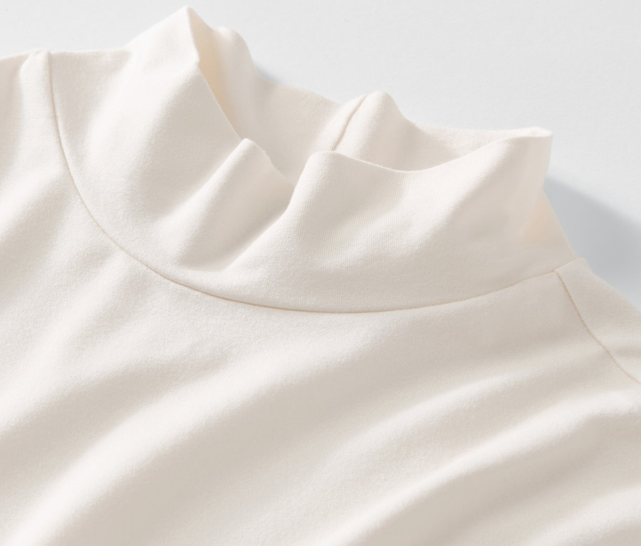 Detailansicht eines cremefarbenen Blusenshirts mit Stehkragen auf weißem Hintergrund.