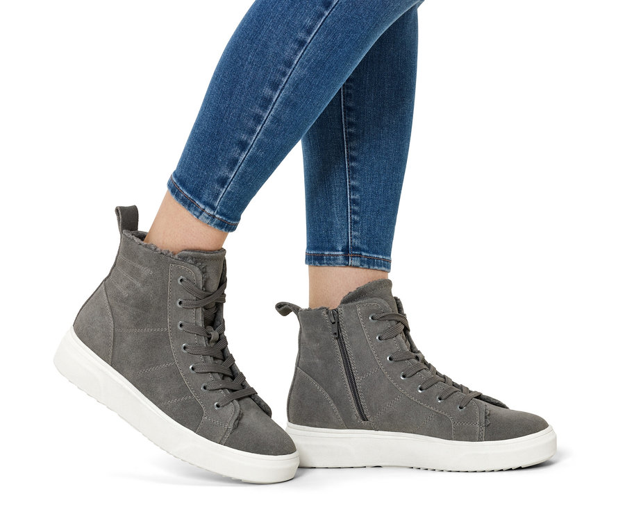 Beine in blauen Jeans und grauen Wildlederstiefeln mit weißen Sohlen.