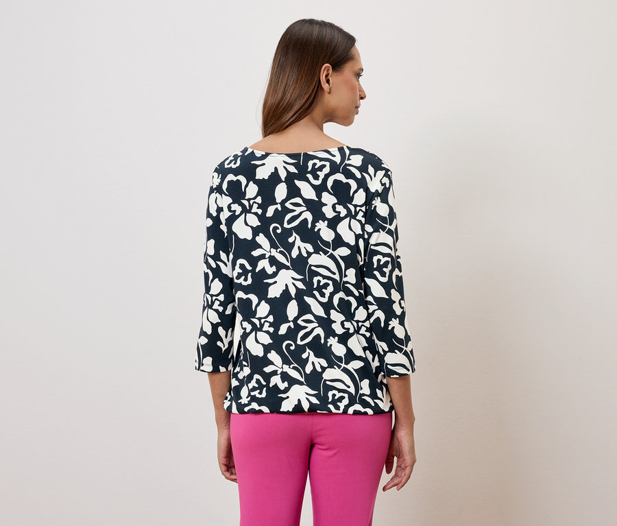 Frau von hinten, trägt eine marineblaue, blumenbedruckte Bluse mit Dreiviertelärmeln und pinkfarbene Hosen.