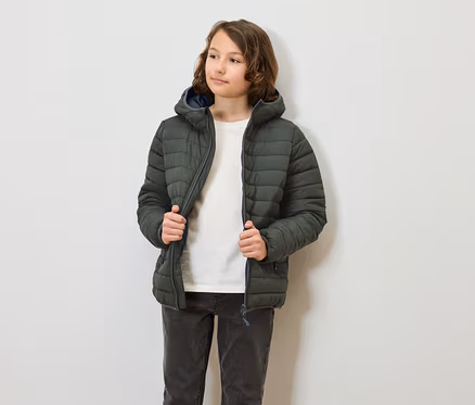 Eine jugendliche Person trägt eine olivgrüne Steppjacke mit Kapuze und schliesst sie. Die Person trägt Jeans und ein T-Shirt.