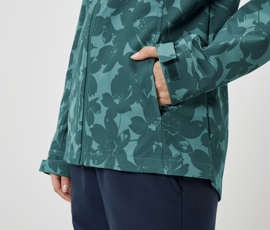 Person mit Hand in der Tasche einer grün-blau gemusterten Jacke, dazu blaue Hose.