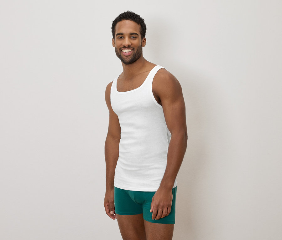 Dunkelhäutiger Mann, der ein weißes Tanktop und grüne Boxershorts trägt und lächelt.