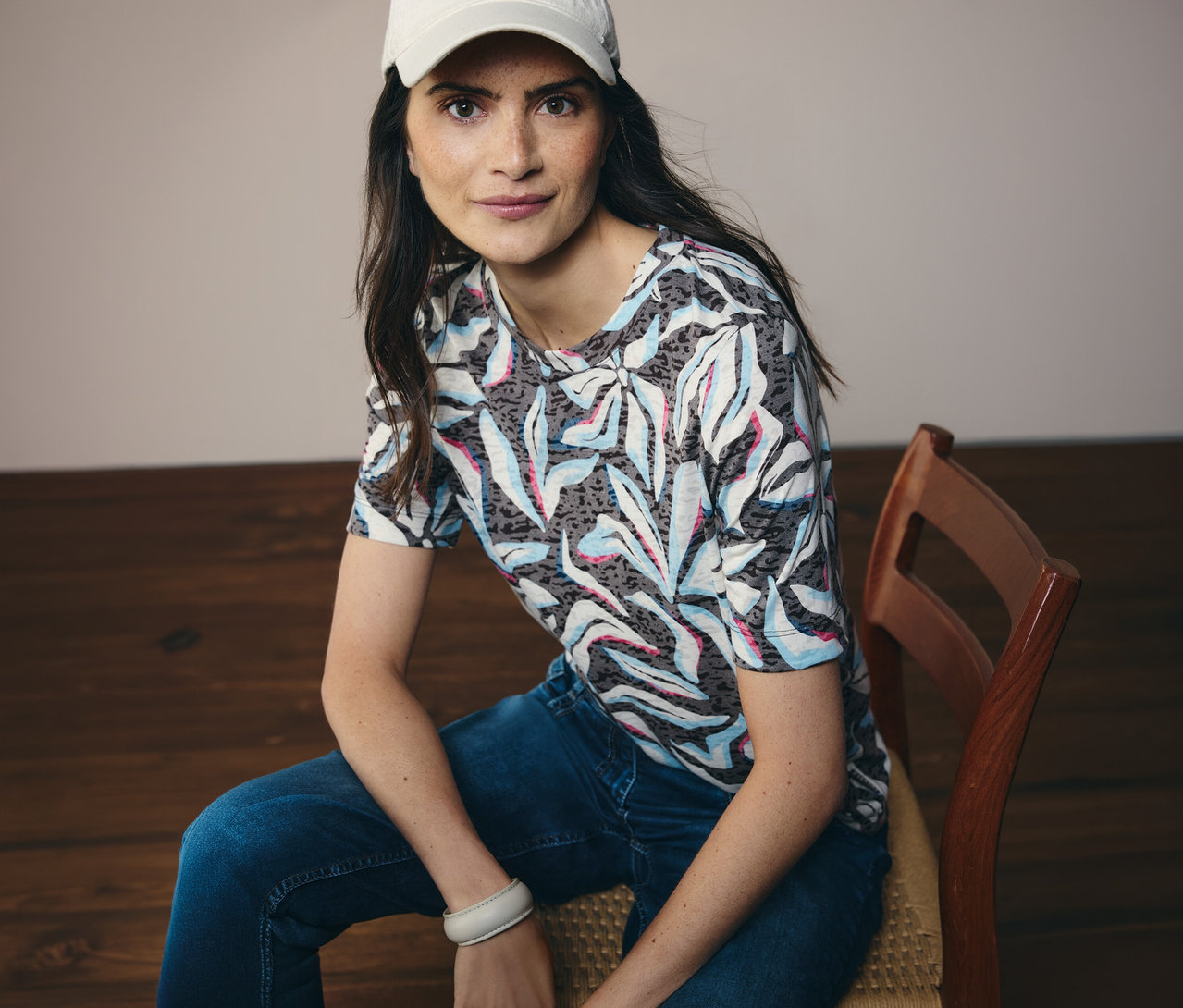 Frau mit weißer Kappe sitzt und trägt ein blaues CECIL Kurzarmshirt mit Muster.