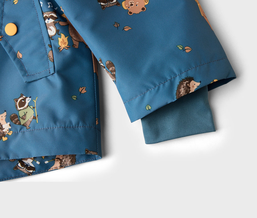 Detailansicht einer blaugrünen Jacke mit Tiermuster, darunter Waschbären, Bären und Igel, sowie Blätter und Lagerfeuer.