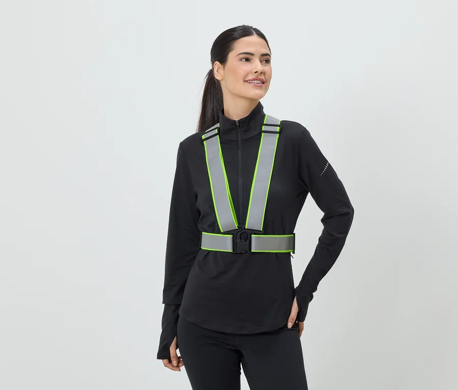 Frau mit Pferdeschwanz trägt eine reflektierende Sicherheitsweste mit neongrünen Akzenten über einem schwarzen Sportoberteil.