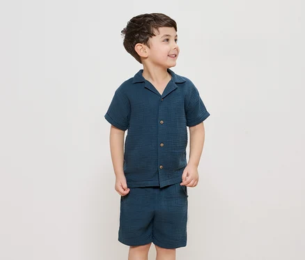 Ein Junge trägt ein marineblaues Hemd mit Knöpfen und dazu passende Shorts.