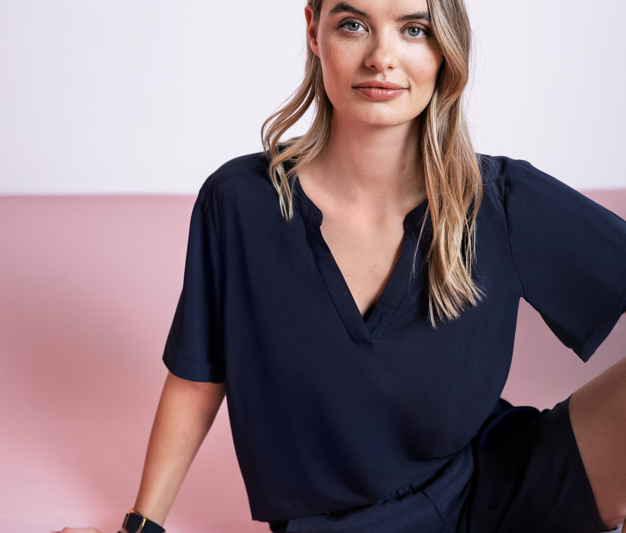 Frau sitzt vor rosa Hintergrund und trägt eine Street One Webbluse in Dunkelblau.