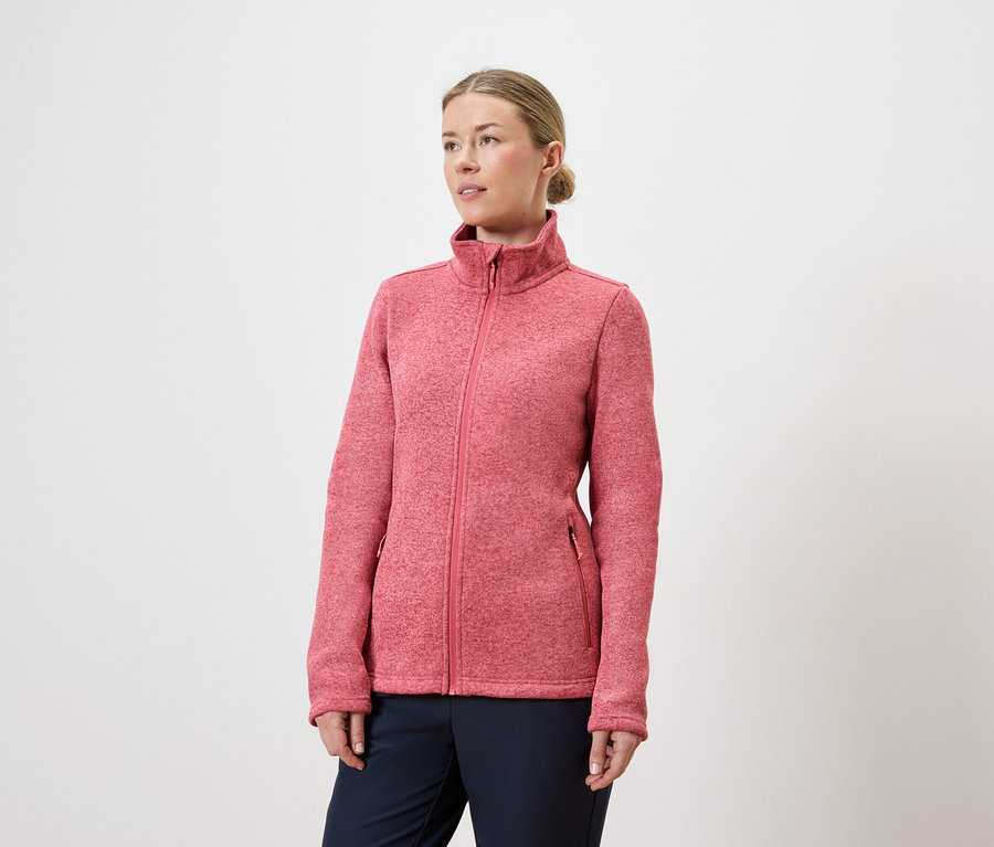 Frau mit Dutt trägt eine pinke Fleecejacke mit Reißverschluss und marineblaue Hose vor einem weißen Hintergrund.