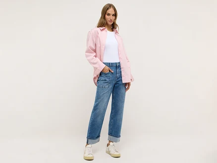 Frau trägt eine helle Hose, ein weißes T-Shirt und ein rosa Hemd.