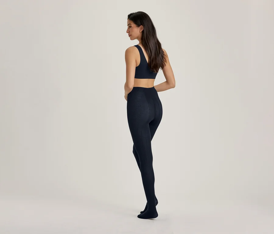 Eine Frau steht mit dem Rücken zum Betrachter, leicht nach links gedreht, trägt einen dunkelblauen Sport-BH und passende dunkelblaue Leggings.
