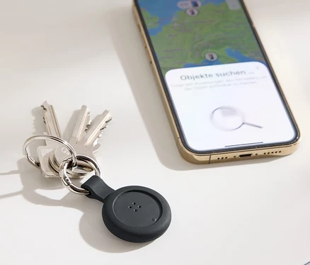 Schlüssel mit schwarzem Tracker und ein Handy mit einer Karte auf dem Display liegen auf einem Tisch.