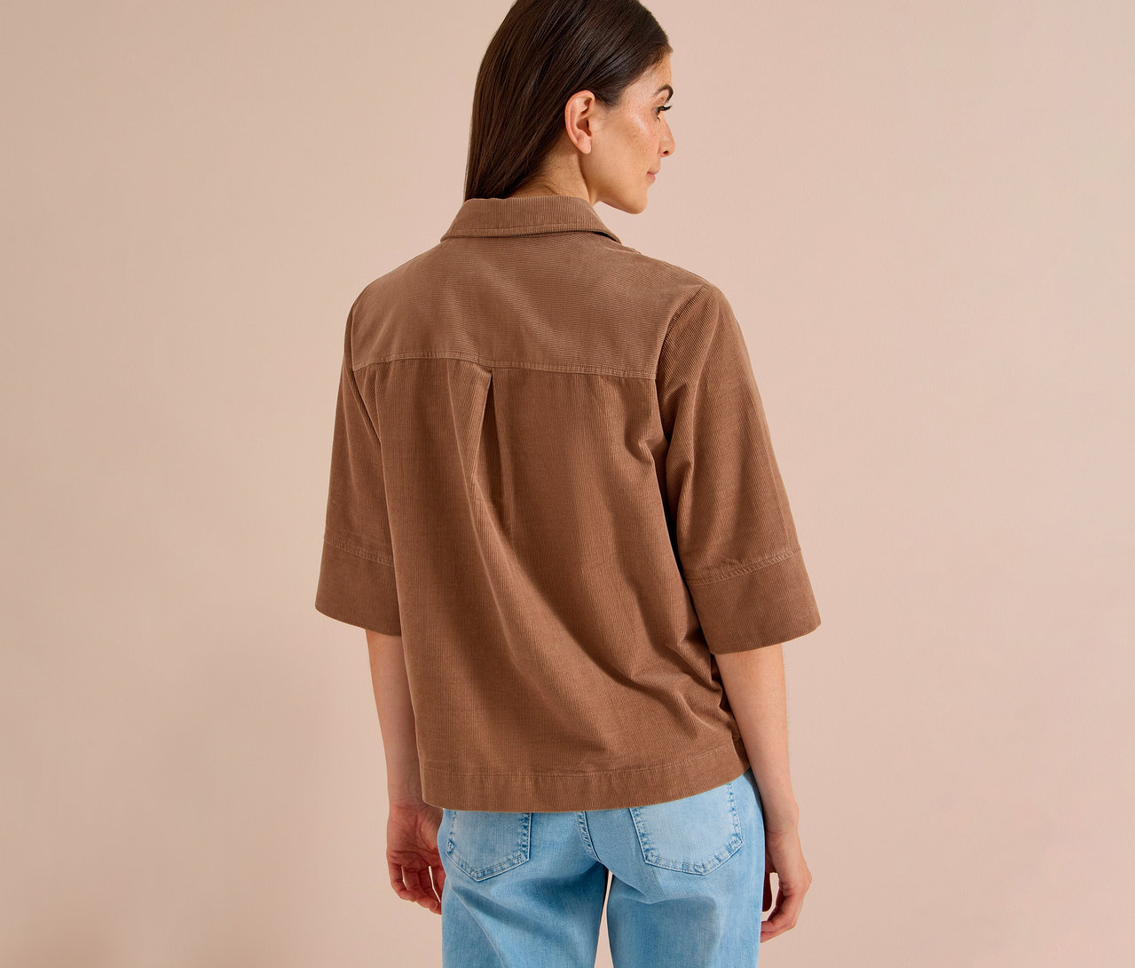 Frau von hinten, die eine braune CECIL Hemdbluse aus Cord und blaue Jeans trägt.