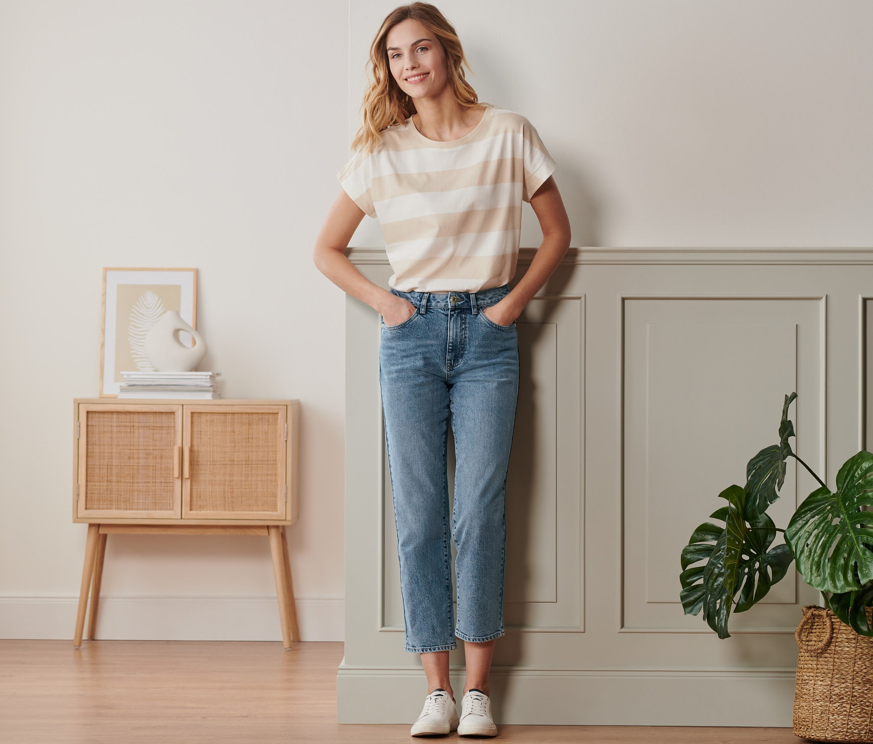 Frau posiert in Straightfit-Jeans, gestreiftem T-Shirt und weißen Schuhen.