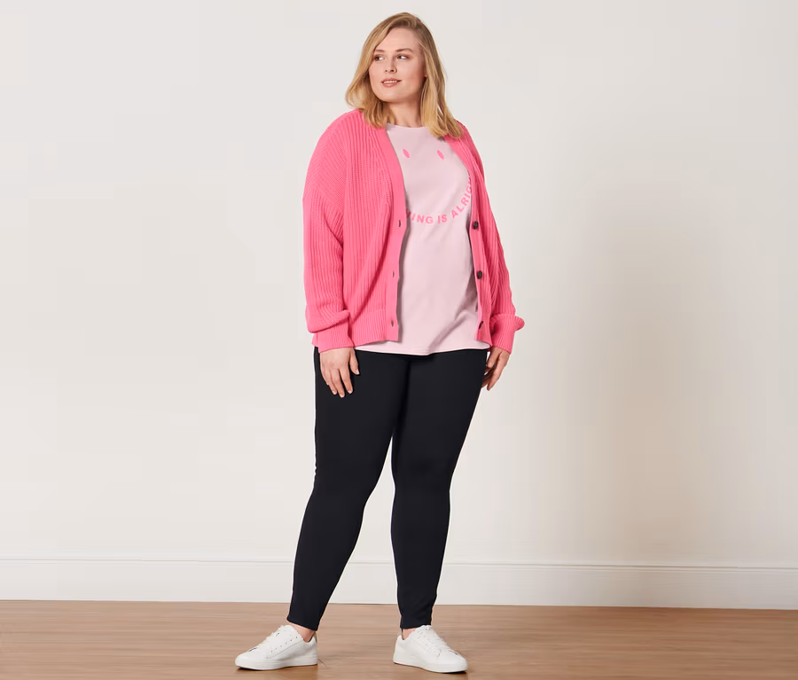 Frau posiert in Jeggings, T-Shirt mit Statement-Print, Ledersneaker und Grobstrick-Cardigan.