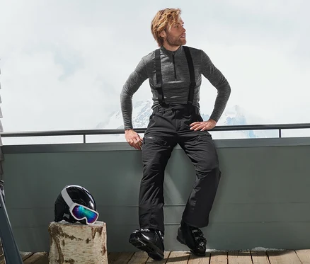 Mann sitzt auf Terrasse in High-Tech-Skihose, daneben liegen Helm und Ski.