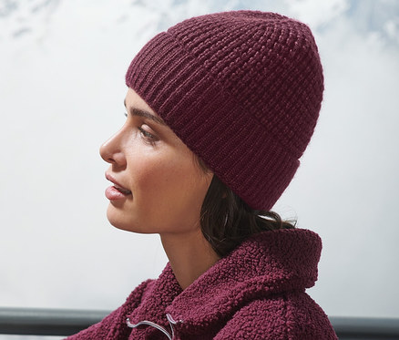 Frau sitzt draußen und trägt eine bordeauxrote Strickmütze.