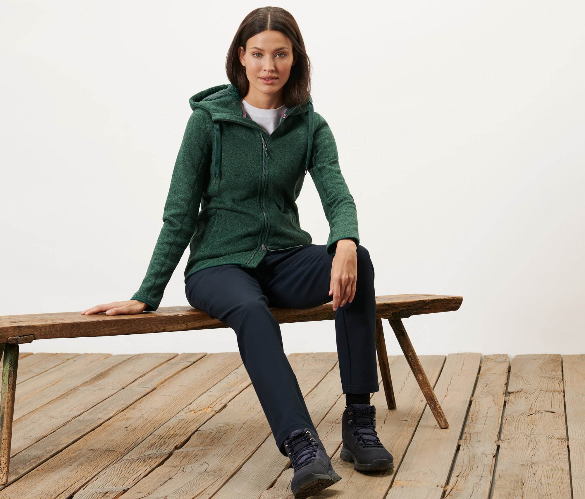 Frau sitzt auf Bank, trägt eine grün melierte Kapuzen-Strickfleecejacke.