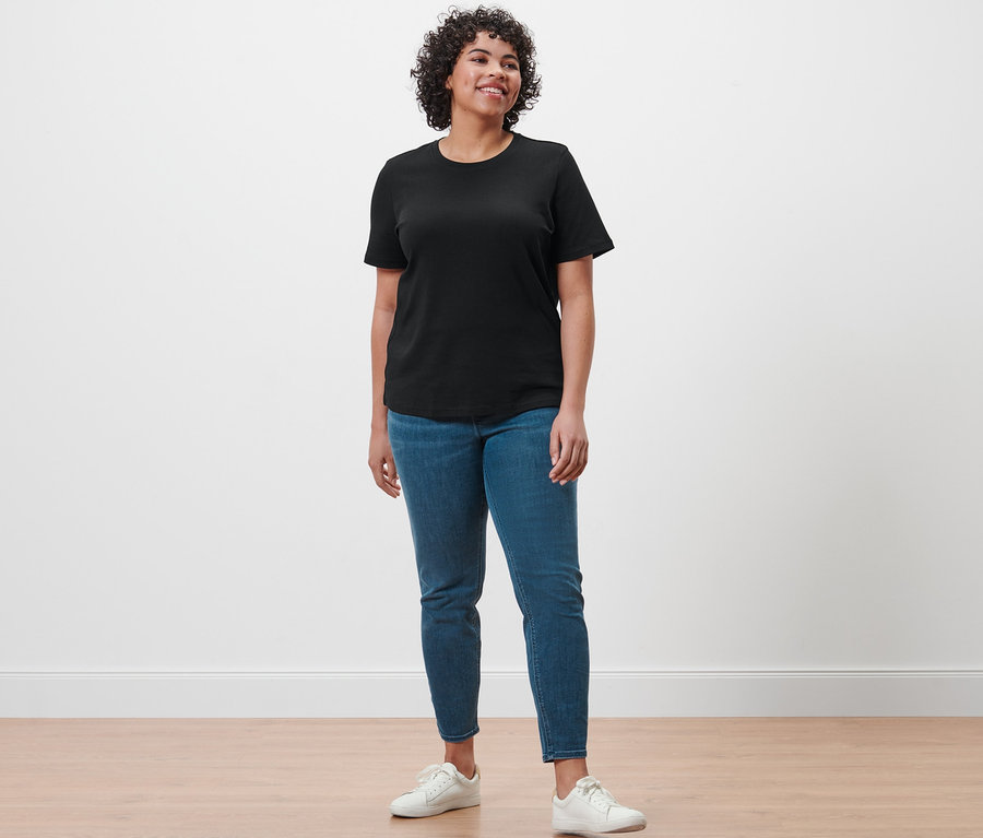 Eine Frau steht und trägt ein schwarzes Basic T-Shirt, Treggings »Fit Nelly« und weiße Turnschuhe.