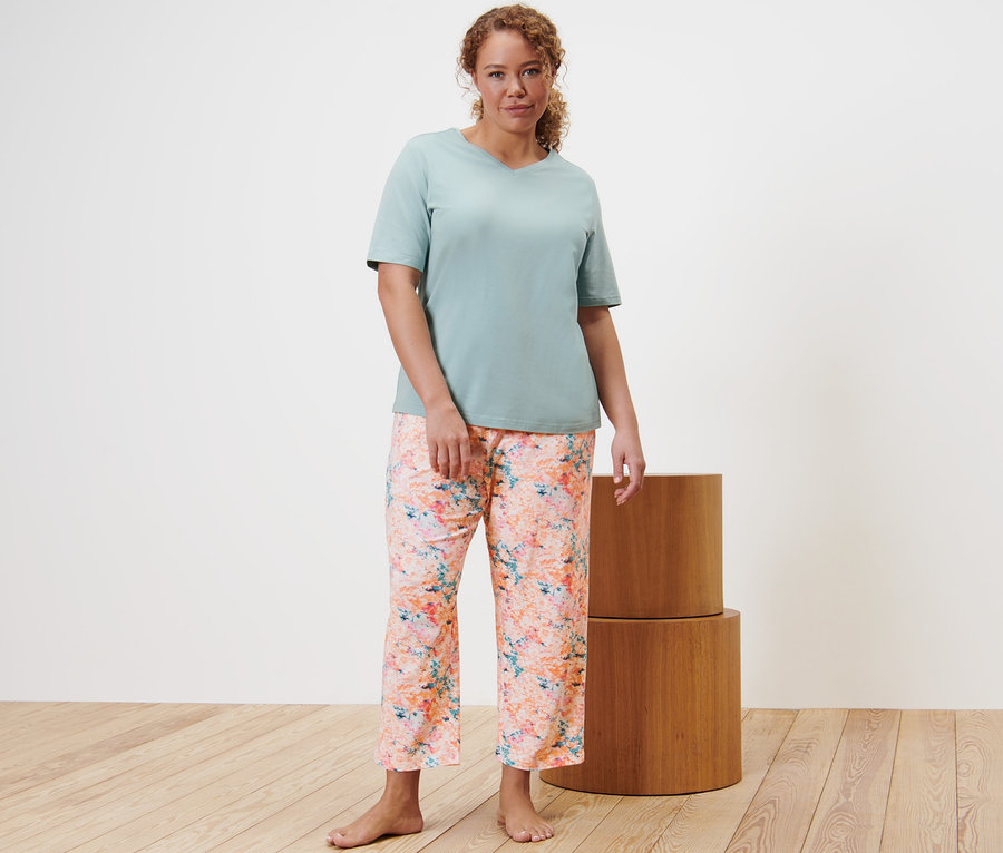Eine Frau steht und trägt einen Pyjama, Hose mit Blumen-Alloverprint und ein T-Shirt.