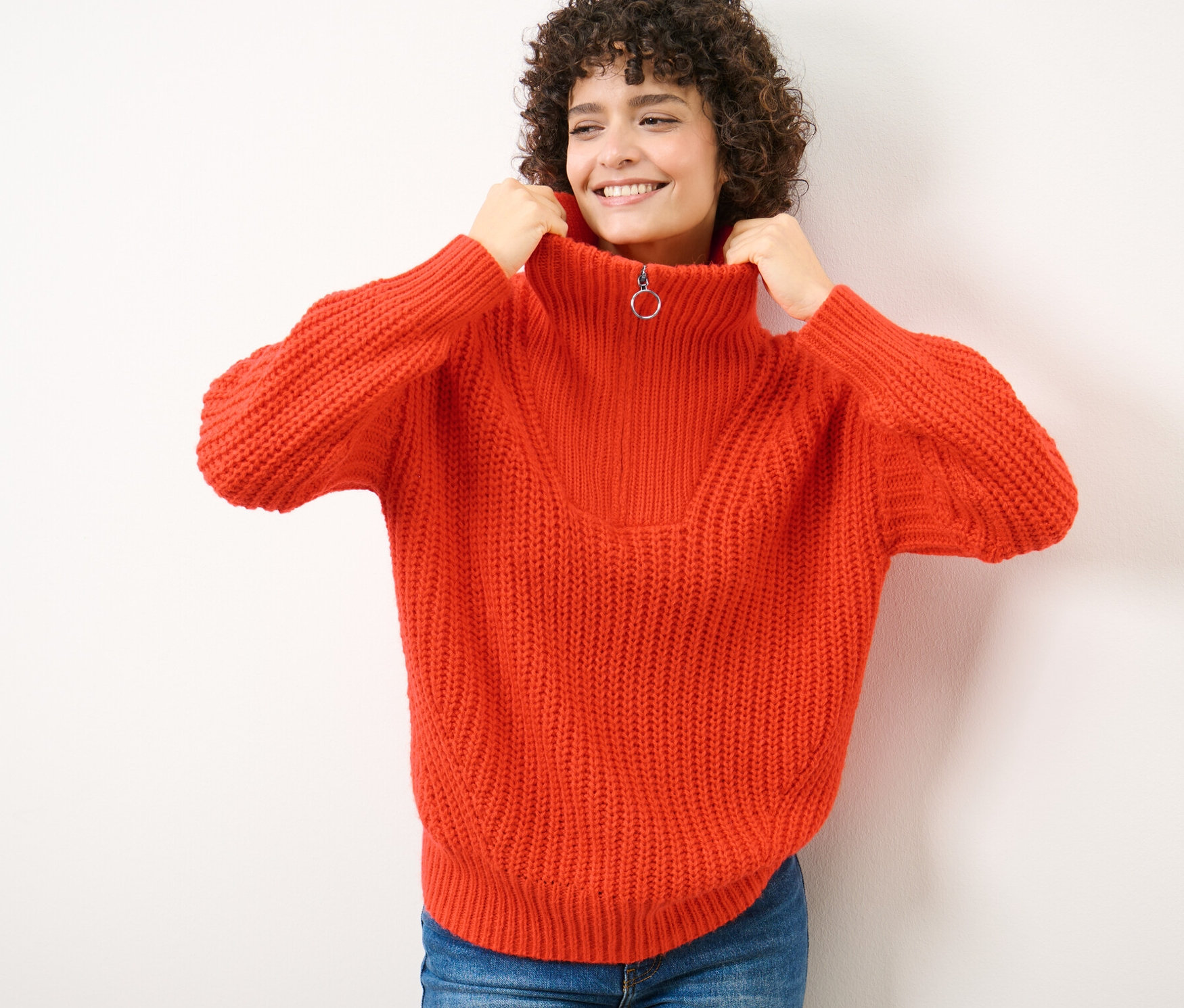 Frau zieht den Kragen eines orangefarbenen Grobstrick-Troyers an ihren Hals.