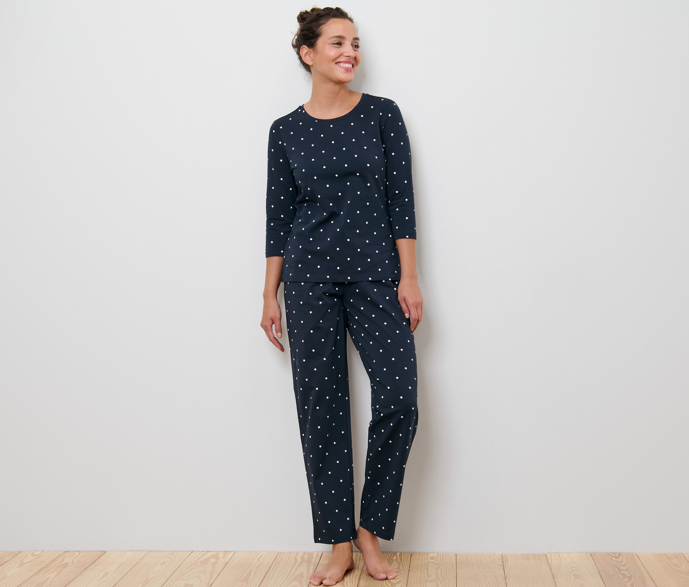 Frau steht und trägt einen dunkelblauen Pyjama mit Punkten.
