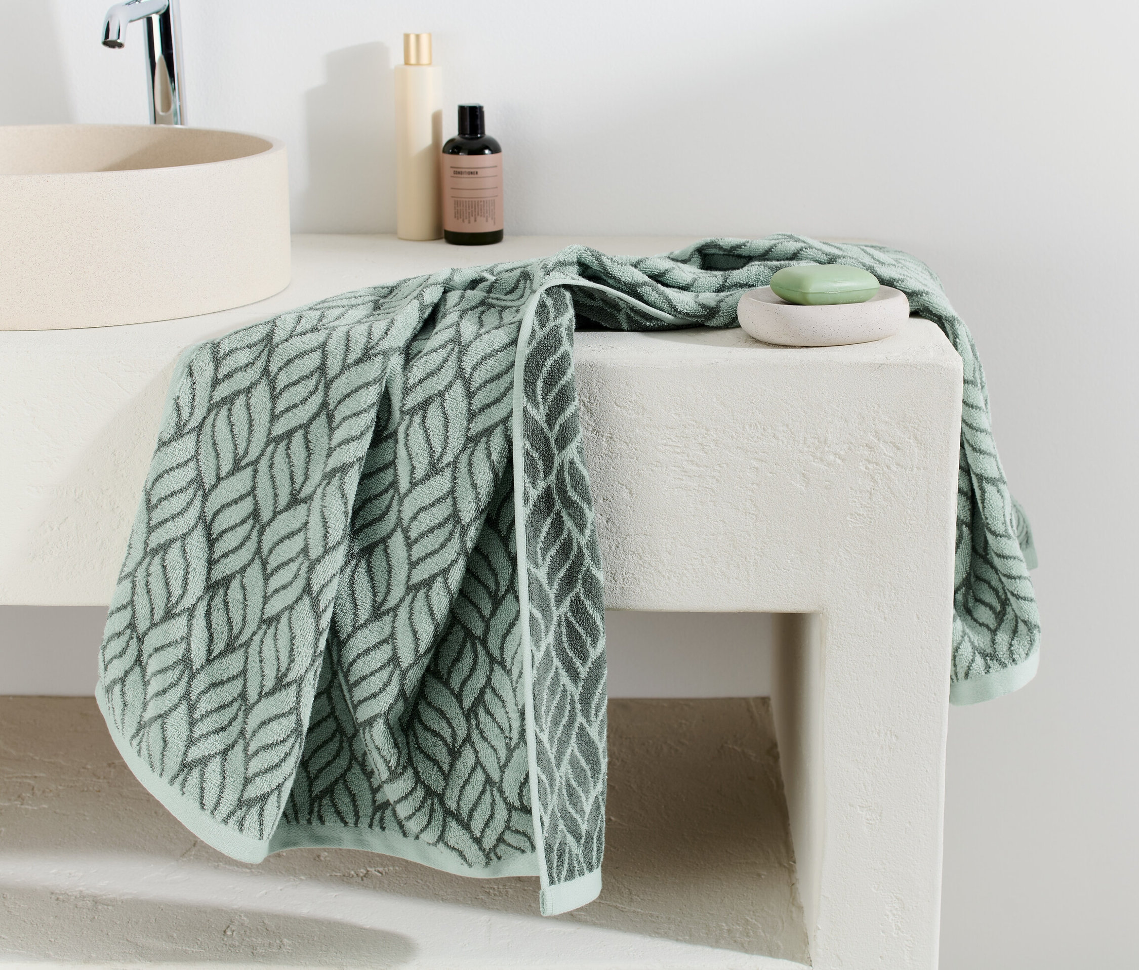 Ein Jacquard-Badetuch mit Blattmuster liegt auf einer weißen Waschtischplatte.