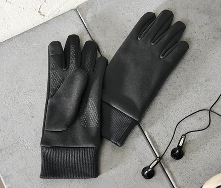 Zwei Kinder-Windprotection-Thermohandschuhe liegen auf einer grauen Oberfläche neben Kopfhörern und einem Teil eines Fußballs.