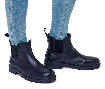 Beine in Jeans und Regenstiefeletten.
