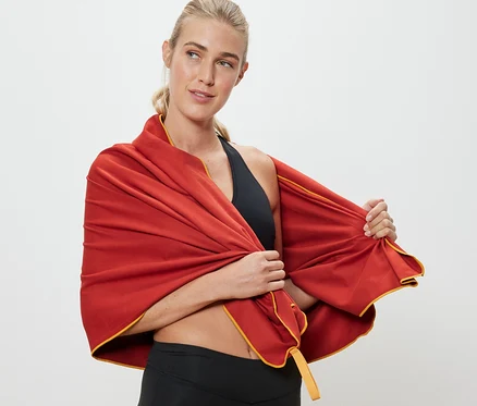 Blonde Frau drapiert ein orangefarbenes Outdoor-Handtuch, ca. 70 x 140 cm, um ihre Schultern.
