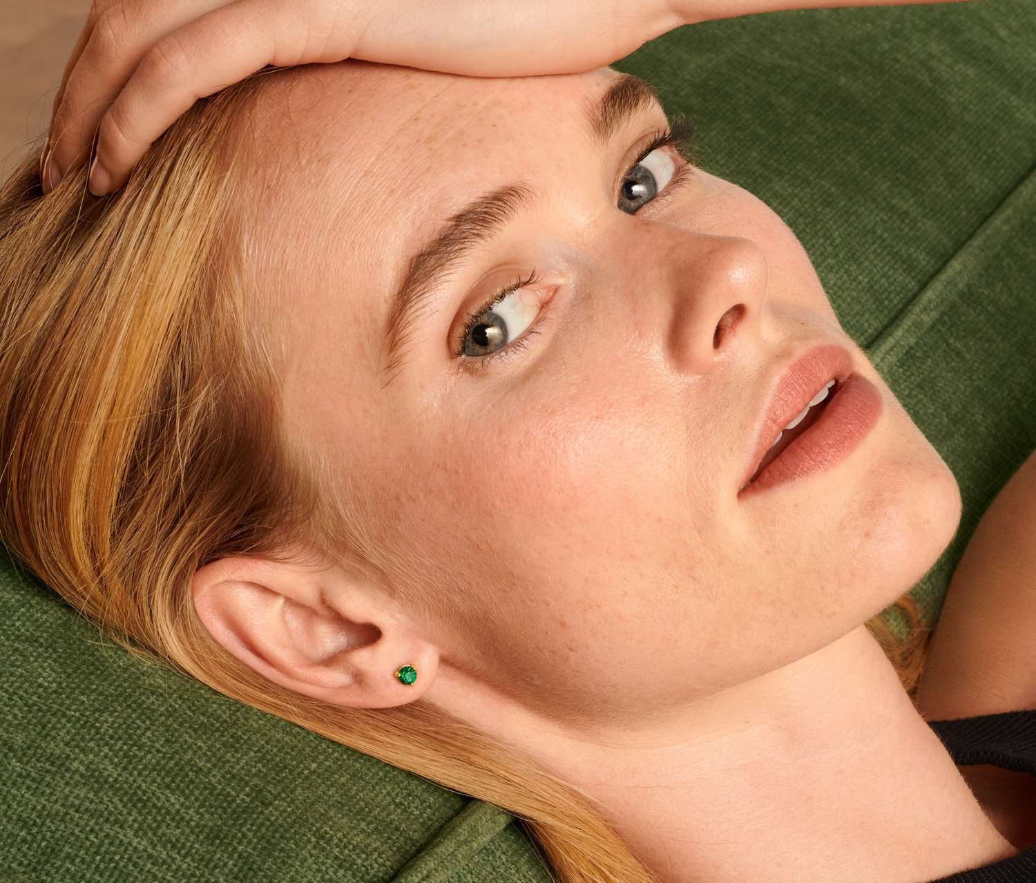 Blonde Frau liegt auf einem grünen Sofa und trägt ein Ohrstecker Set.