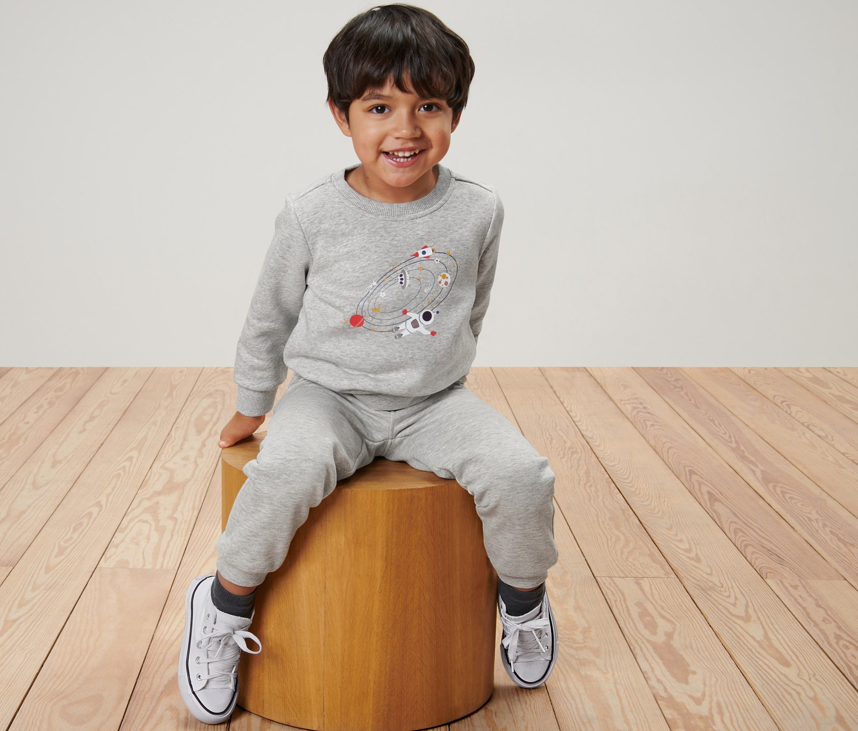 Junge sitzt auf einem Hocker und trägt einen Kinder-Sweater, Outerspace.