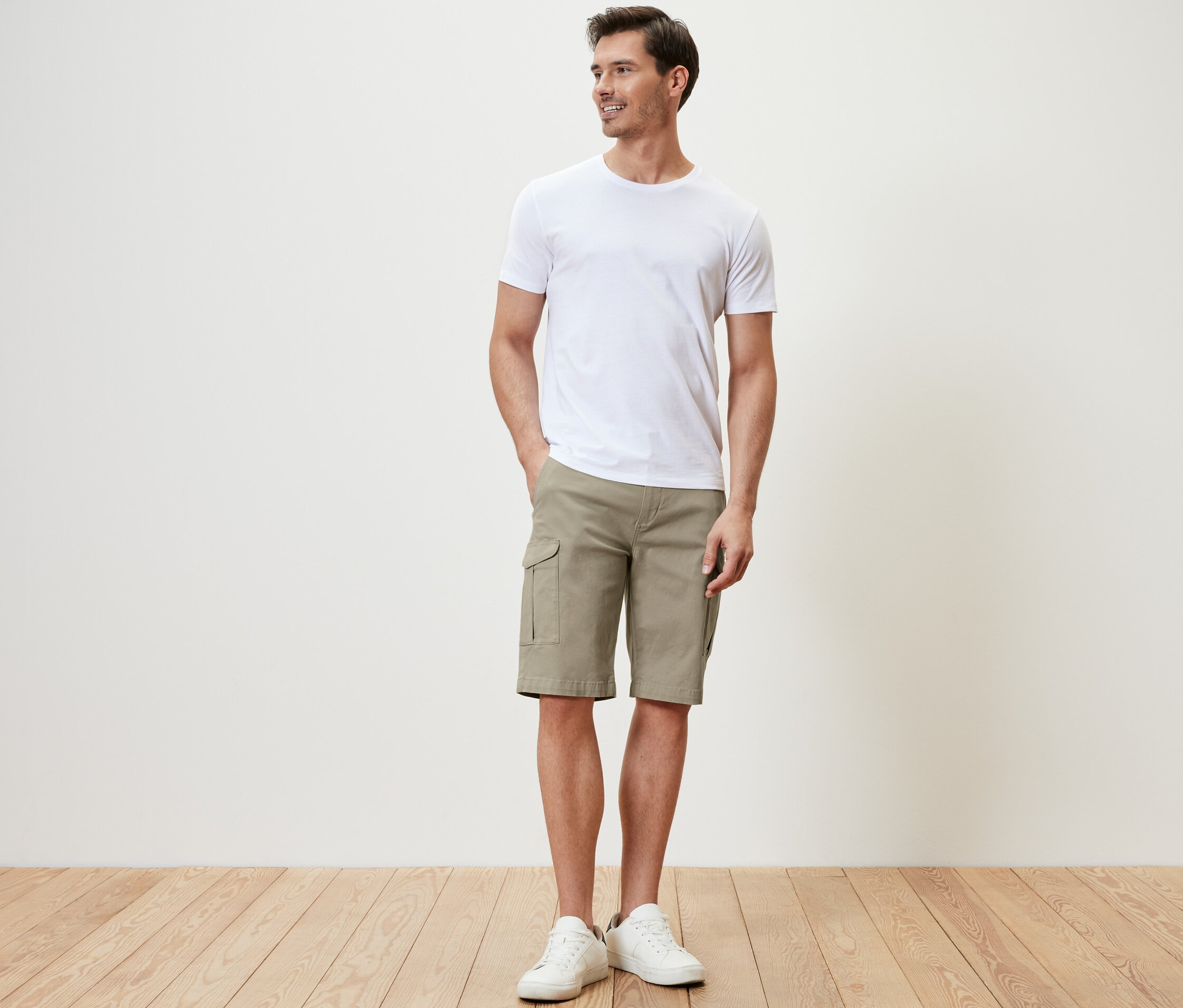 Mann steht und trägt beige Cargo-Shorts und ein weißes T-Shirt.