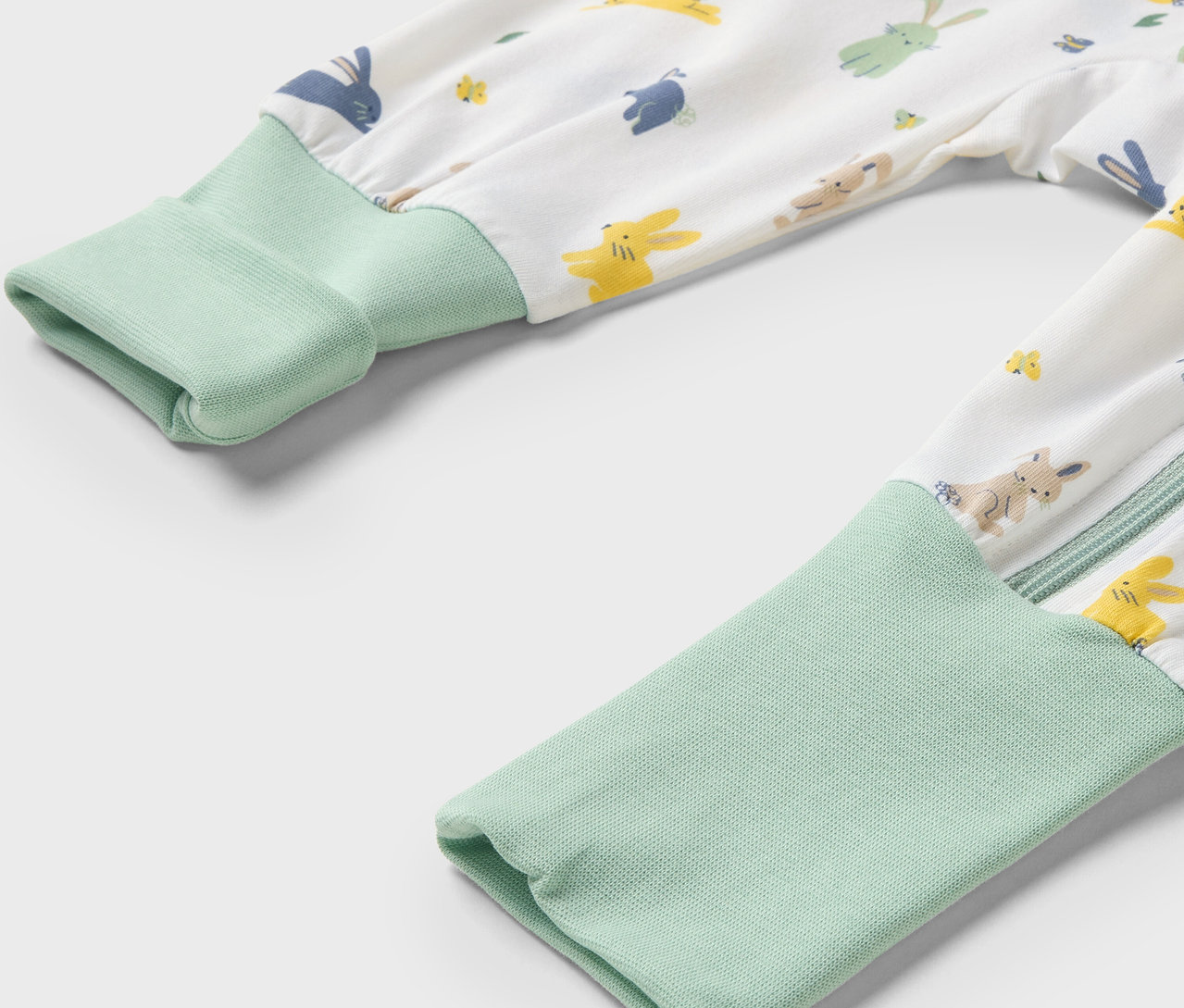 Detailaufnahme eines Baby-Overalls mit Hasenmuster und hellgrünen Bündchen an den Ärmeln.