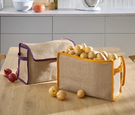 Zwei beige Körbe stehen auf einem Tisch, einer mit lila Rand ist leer und der andere mit orangefarbenem Rand ist mit Kartoffeln gefüllt.