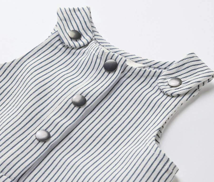Detailaufnahme einer Kinder-Web-Latzhose mit blauen Streifen und silbernen Knöpfen.