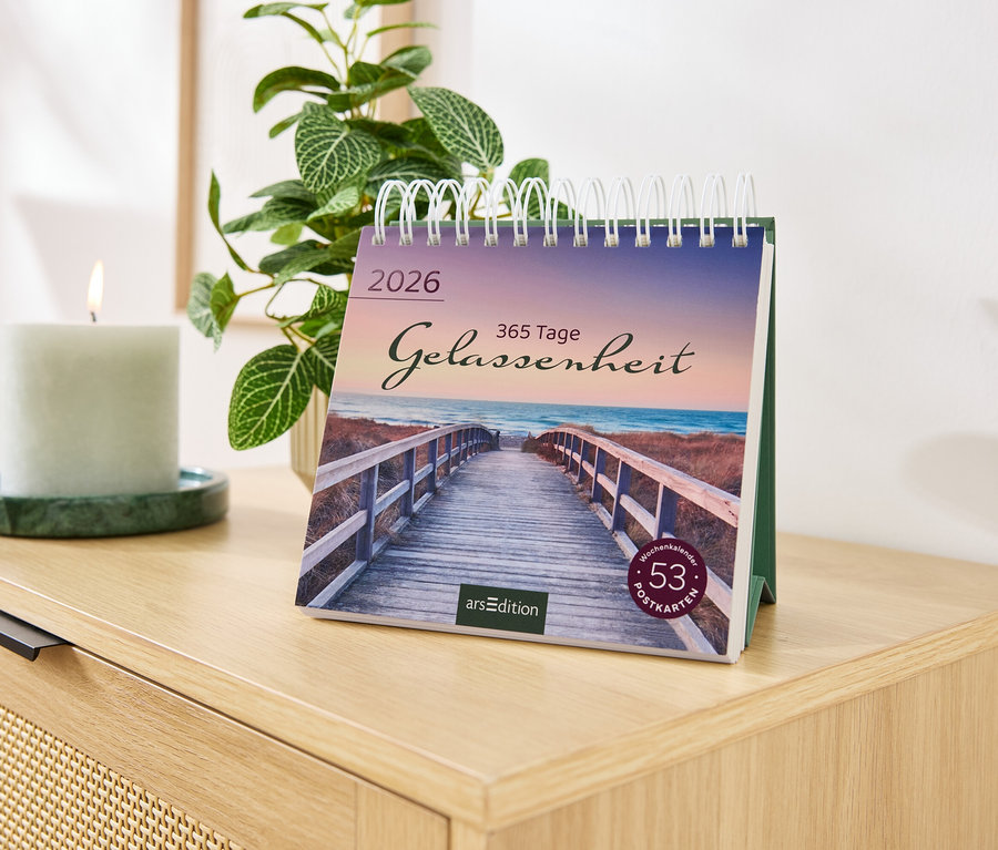 Auf einer Kommode stehen ein Kalender mit der Aufschrift Gelassenheit, eine Kerze und eine Pflanze.