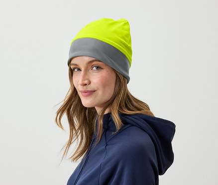 Porträt einer Frau mit braunem Haar und einer grau-gelben Mütze, gekleidet in einem blauen Hoodie.