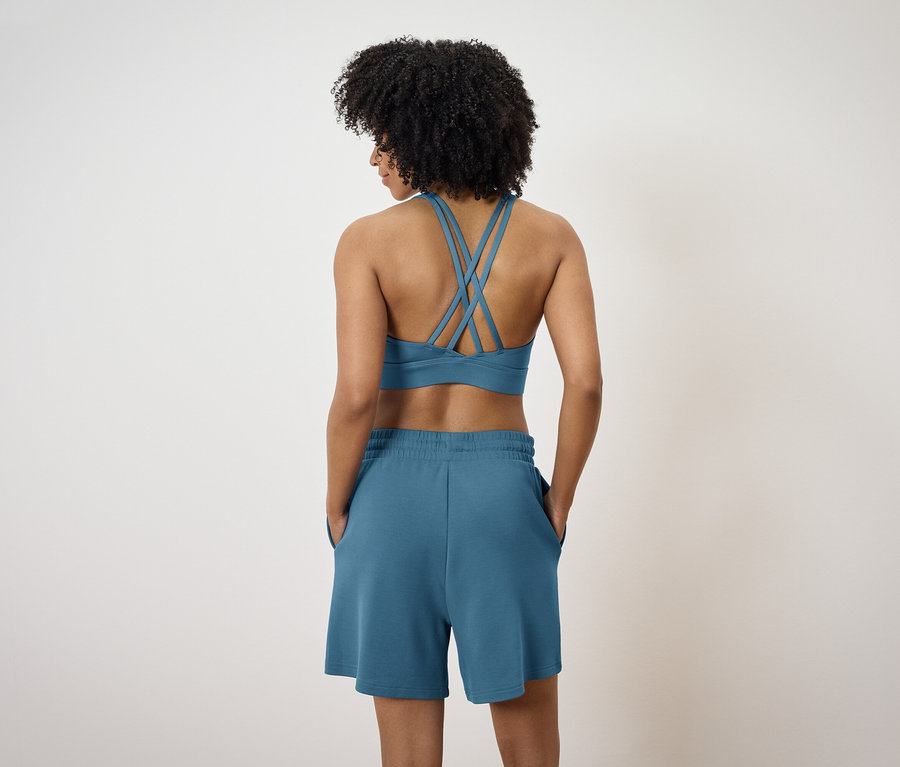 Rückansicht einer Frau mit Afro-Haar, die einen blauen Sport-BH mit gekreuzten Trägern und blaue Shorts trägt.