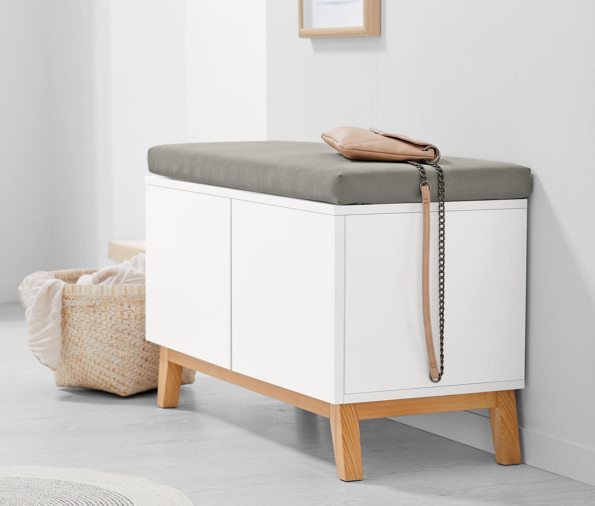 Eine weiße Sitzbank mit Stauraumfächern und grauem Kissen. Auf der Bank liegt eine beige Handtasche.