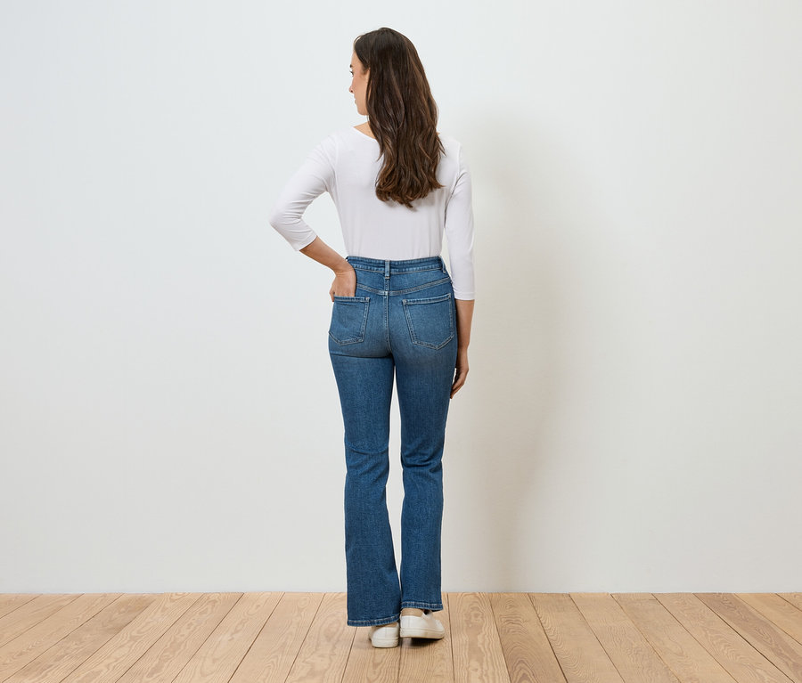 Frau mit dem Rücken zur Kamera, die Hand in der Tasche ihrer blauen Jeans und einem weißen Langarmshirt.